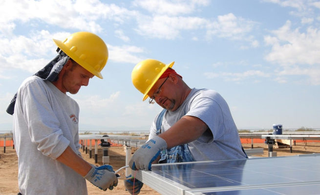 Two men working on a roof wearing hardhats.