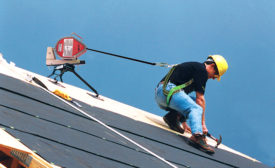 A roofer hooked onto a harness working on a steep slope roof.