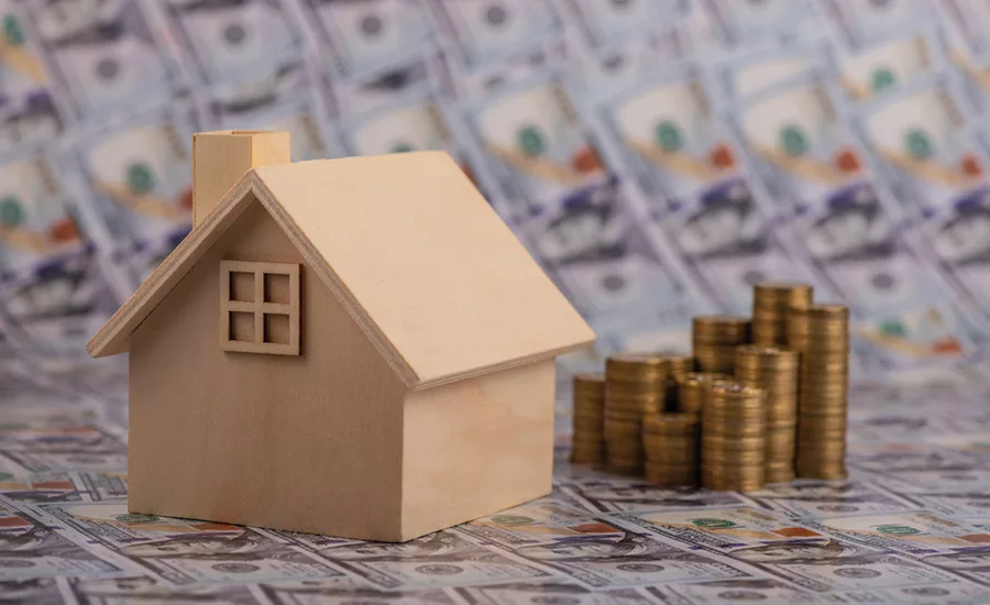 A wooden house model and a stack of coins