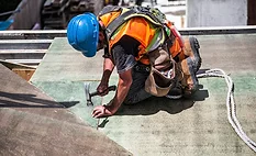 worker-in-safety-gear-hammering-nails-into-roof