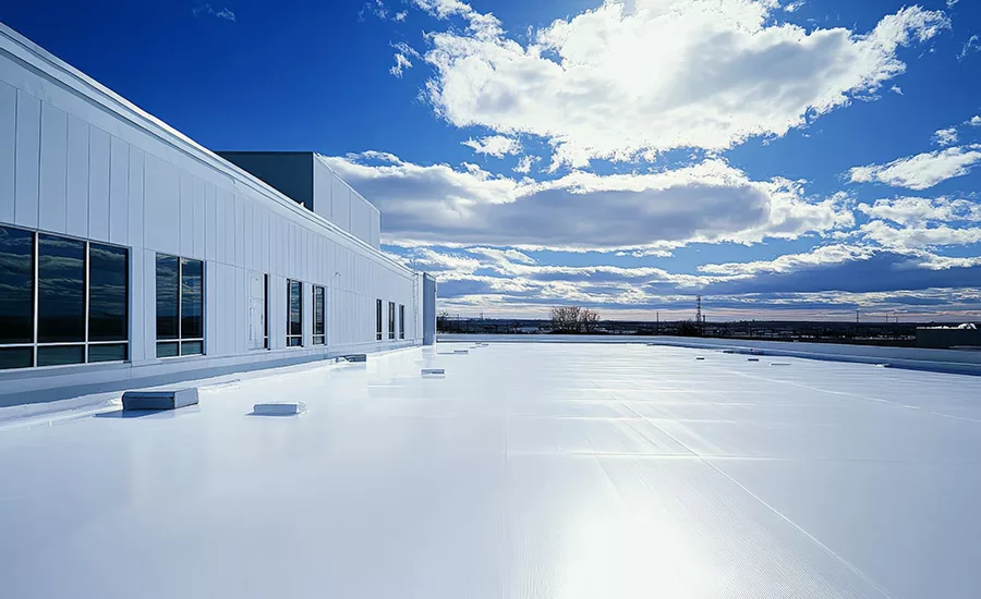 A white commercial roof under a blue sky on a partly cloudy day