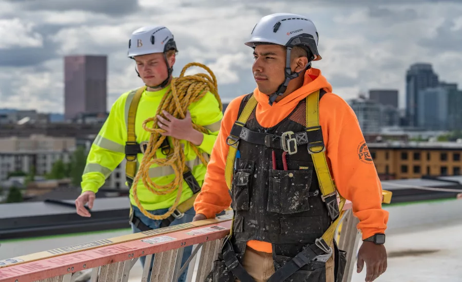 construction-workers-on-roof-in-helmets-carrying-equipment