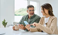 Happy mature couple using phone holding credit card making payments. Middle aged older man and woman doing ecommerce shopping on smartphone booking or buying online on mobile sitting at home table.