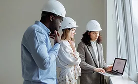 3 architects wearing hard hats looking at a laptop