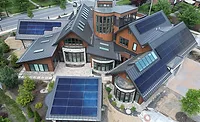 Aerial view of a large, modern house with multiple solar panel arrays on its metal roof