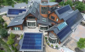 Aerial view of a large, modern house with multiple solar panel arrays on its metal roof