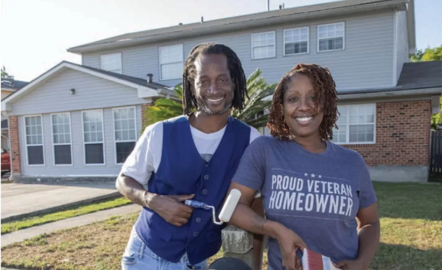 Homeowners stand beside their house with a newly installed roof after hurricane repairs improved storm protection.