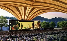 Rendering of Vancouver's Freedom Mobile Arch amphitheater showing a large crowd beneath the sweeping mass-timber roof with mountains visible beyond the stage.