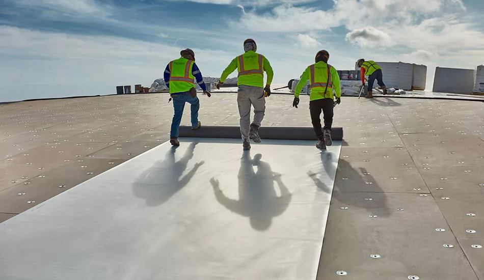 3 roofers unrolling a roofing membrane
