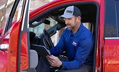A man wearing a TAMKO hat sitting in a red pickup truck
